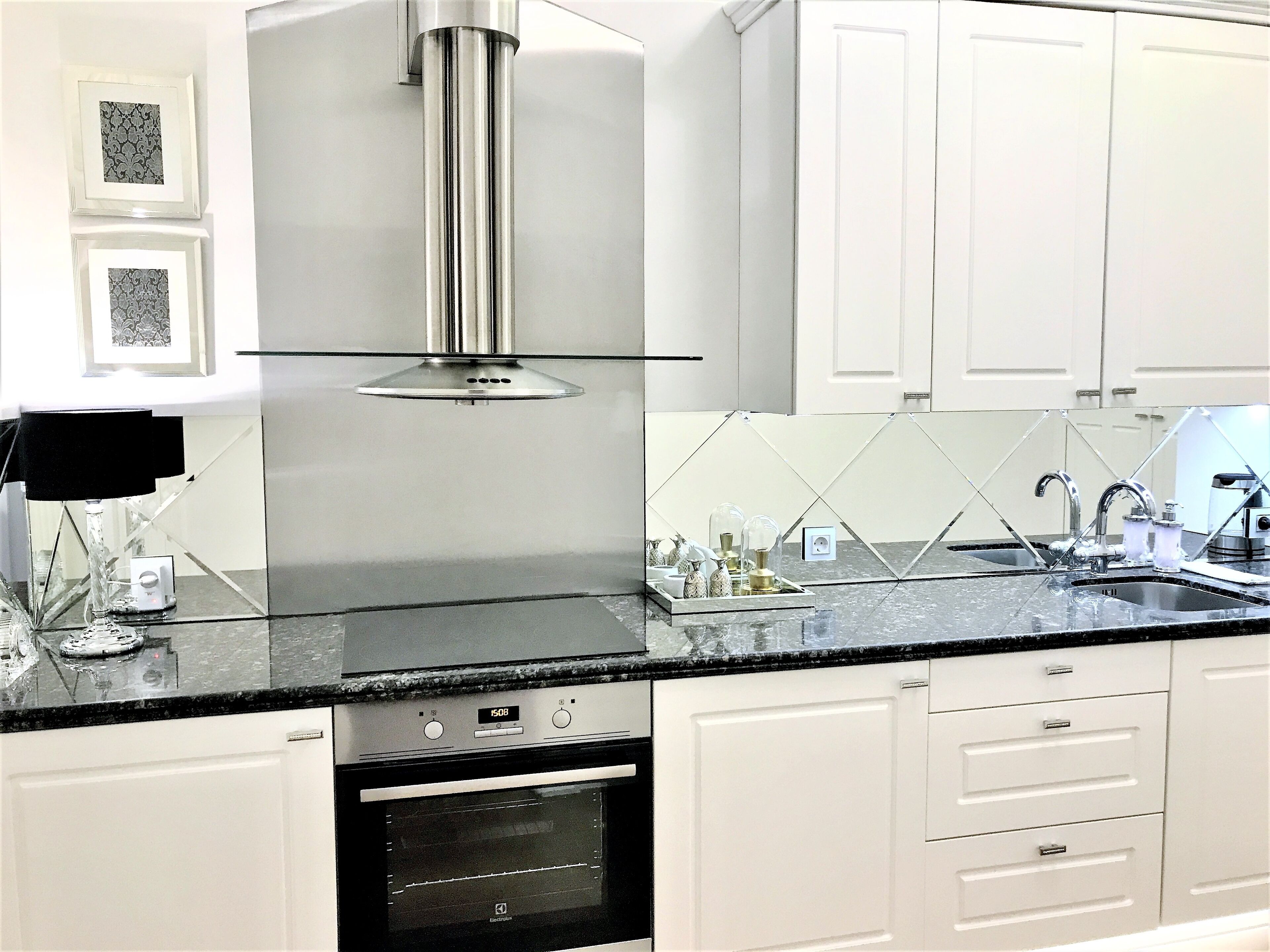 Una cocina moderna con armarios blancos, una campana extractora de acero inoxidable, una encimera negra y un horno empotrado.