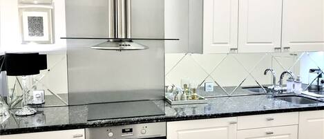 A modern kitchen with white cabinetry, a stainless steel range hood, a black countertop, and a built-in oven.