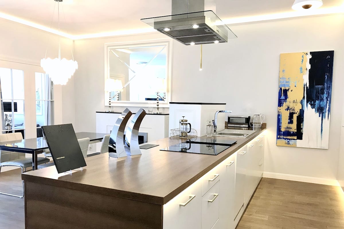 Una cocina moderna con una isla central, armarios blancos y un ventanal amplio.