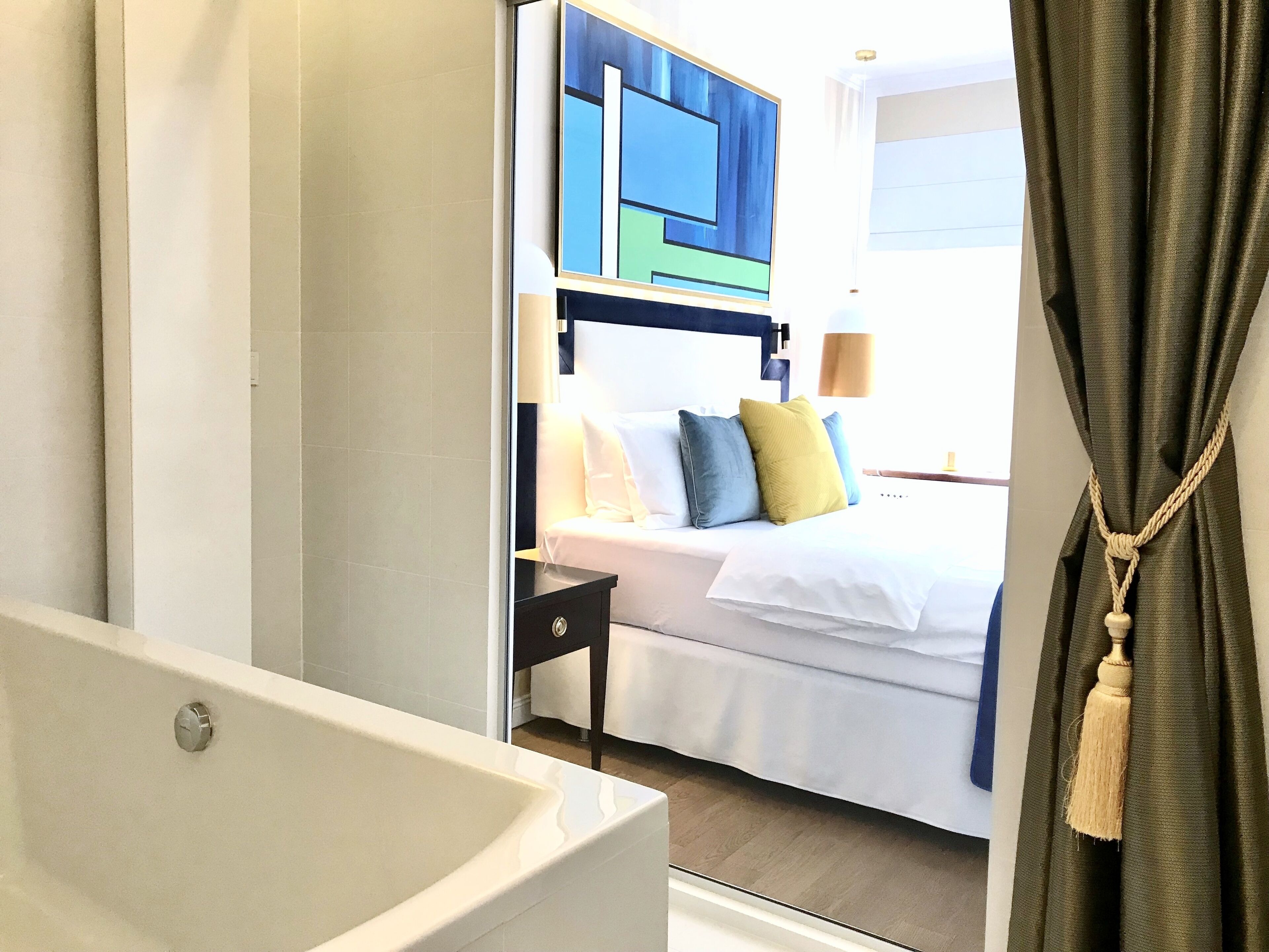 A hotel room with a bathtub, a bed with multiple pillows, and a nightstand.