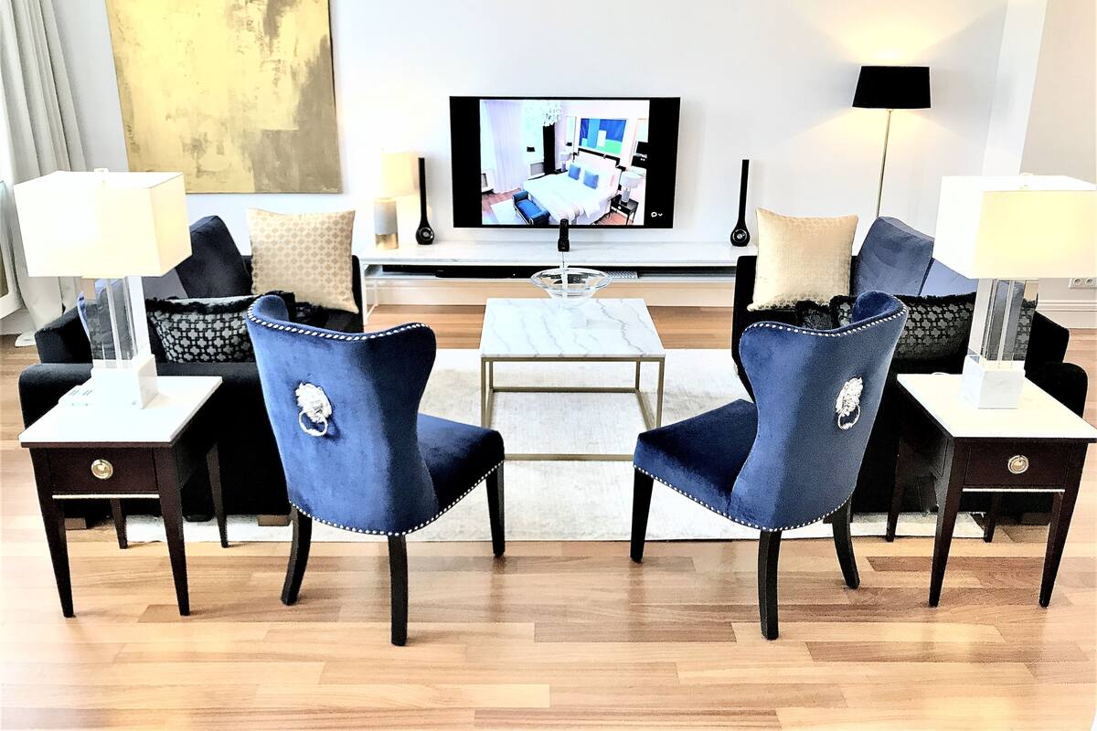 Una sala de estar moderna con un televisor de pantalla plana, dos sillones azules, una mesa de centro y una mesita de noche con una lámpara.