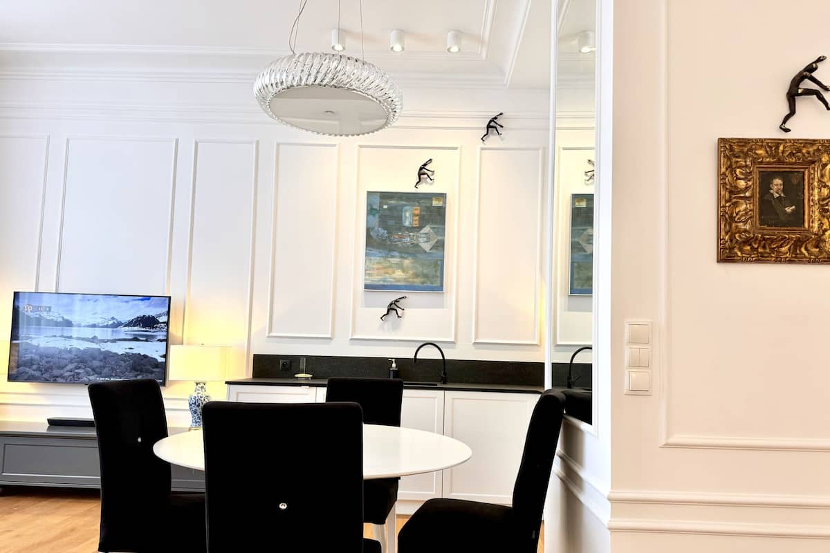 Un comedor moderno con una mesa blanca, sillas negras, una araña y obras de arte en las paredes.