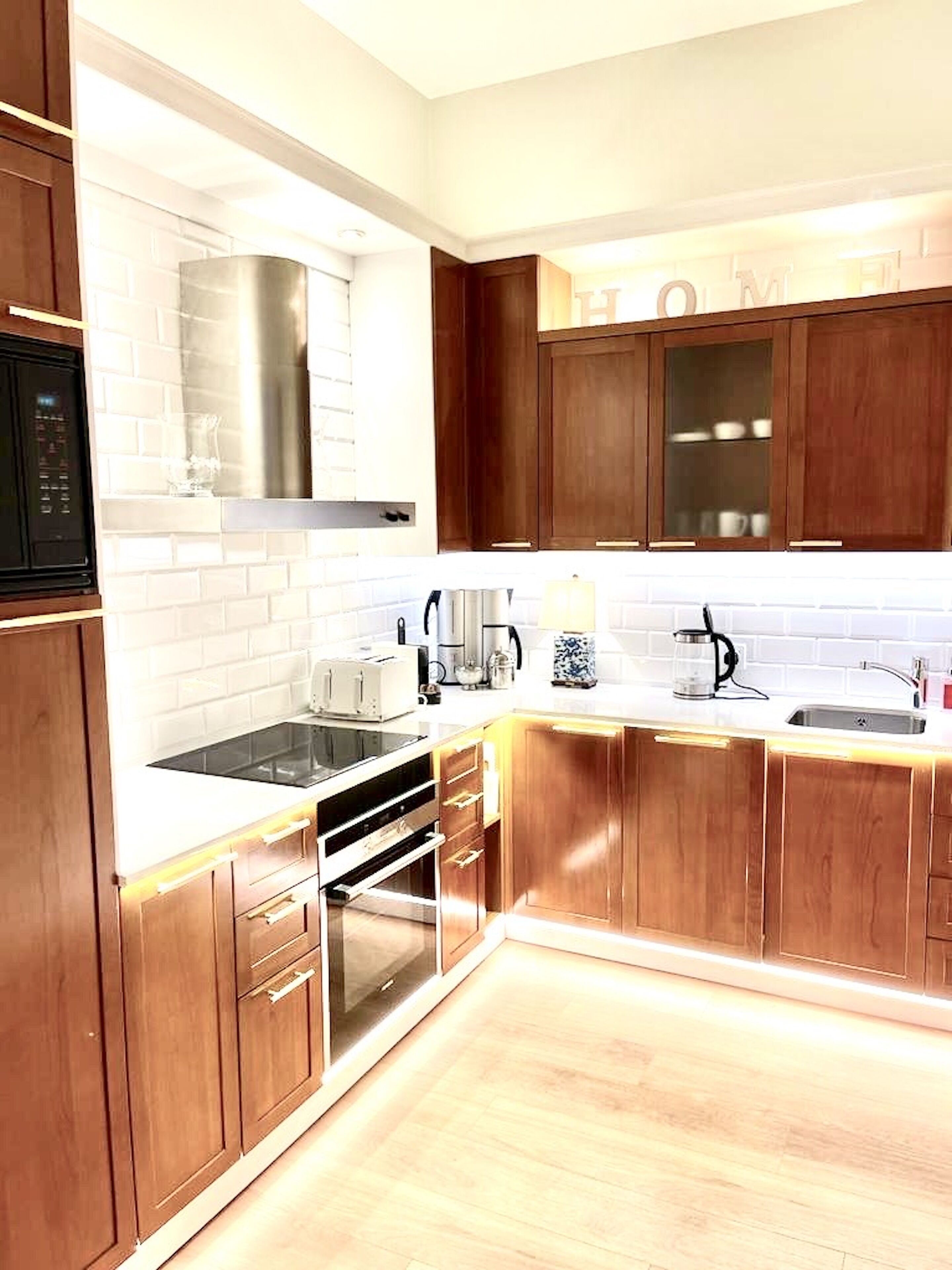 Une cuisine moderne avec des meubles en bois, des plans de travail blancs, une hotte en acier inoxydable et un four encastré.