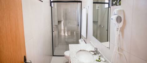 Un bagno con box doccia in vetro, lavandino bianco e asciugacapelli montato a parete.