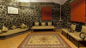 A stone-walled room with a sofa, armchairs, and a patterned rug. - Nisarg Resort (Madale)