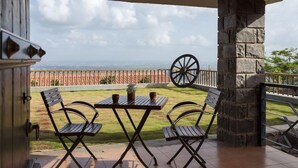 A covered patio with a table and chairs, a stone pillar, and a view of the ocean. - Nisarg Resort (Madale)
