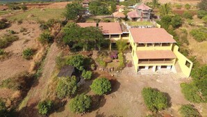 A residential area with multiple houses, some with red roofs and others with green roofs, surrounded by greenery and open fields. - Nisarg Resort (Madale)