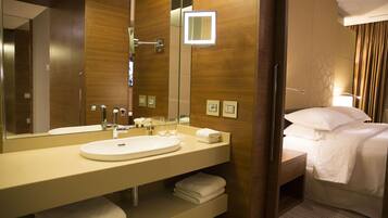A hotel bathroom with a large mirror, a sink, and a bed.