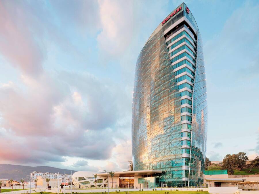 Un hotel moderno con fachada de vidrio curvada, varios balcones y un cartel llamativo en la parte superior.