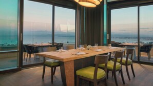 A modern dining area with a large table, chairs, and a view of the city and water. - Sheraton Annaba Hotel (Annaba)