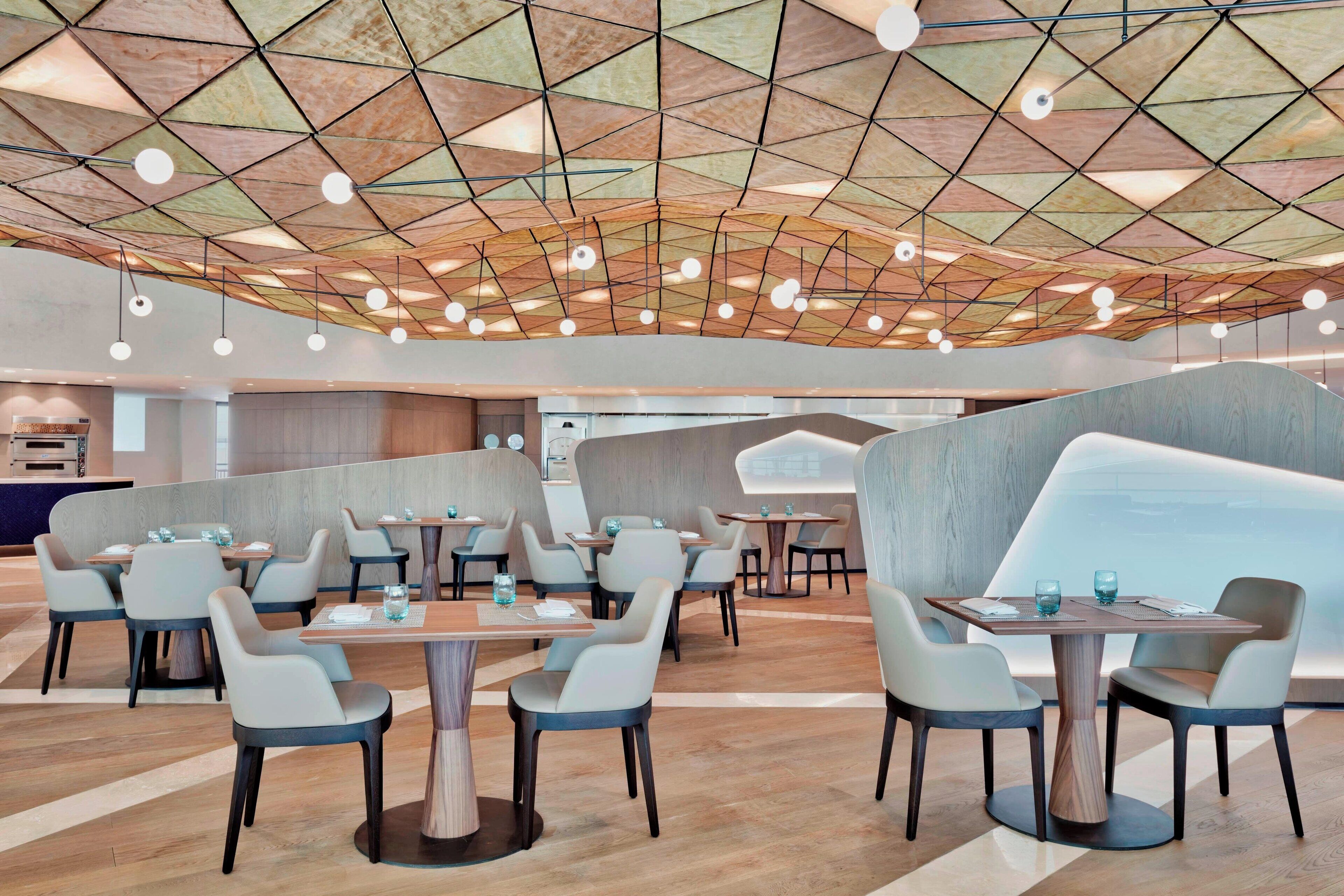 A modern restaurant with geometric ceiling design, round tables, and contemporary chairs.
