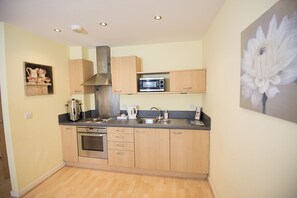 A compact kitchen with wooden cabinets, a stainless steel range hood, a microwave, and a sink.