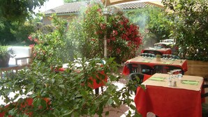 An outdoor dining area with tables covered in red tablecloths, surrounded by lush greenery and flowering plants. - Hotel Saint Louis (Le Thor)
