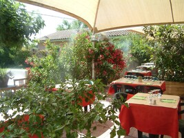 Un espace de restauration en plein air avec des tables recouvertes de nappes rouges, entouré d’une végétation luxuriante et de plantes en fleurs.