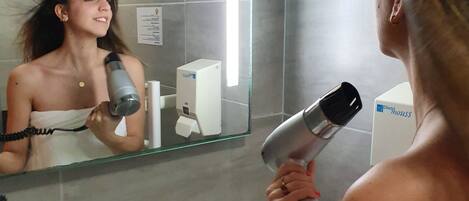 Un baño con espejo, secador de pelo y una toalla colgada en la pared.