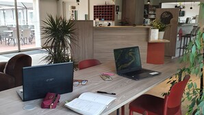 A modern dining area with a wooden table, red chairs, laptops, and a potted plant. - Hotel Saint Louis (Le Thor)