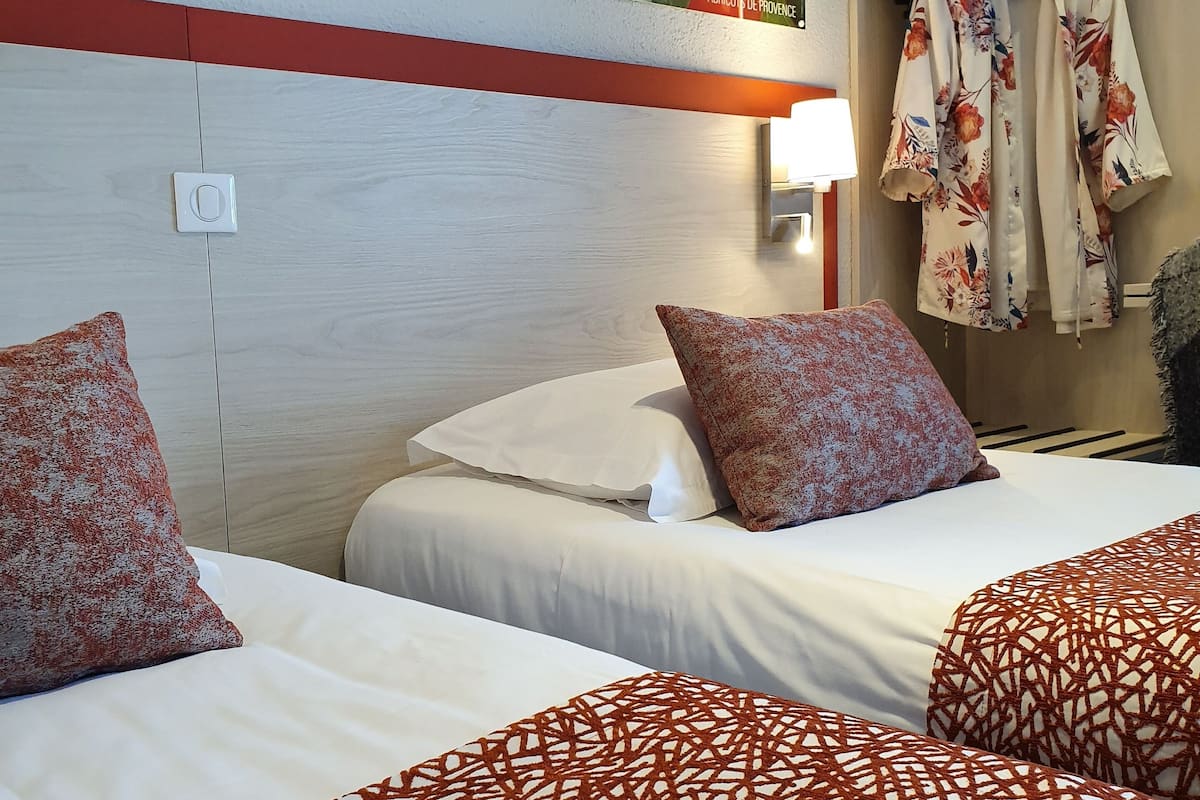 A hotel room with two beds, a wardrobe, and a wall-mounted light.