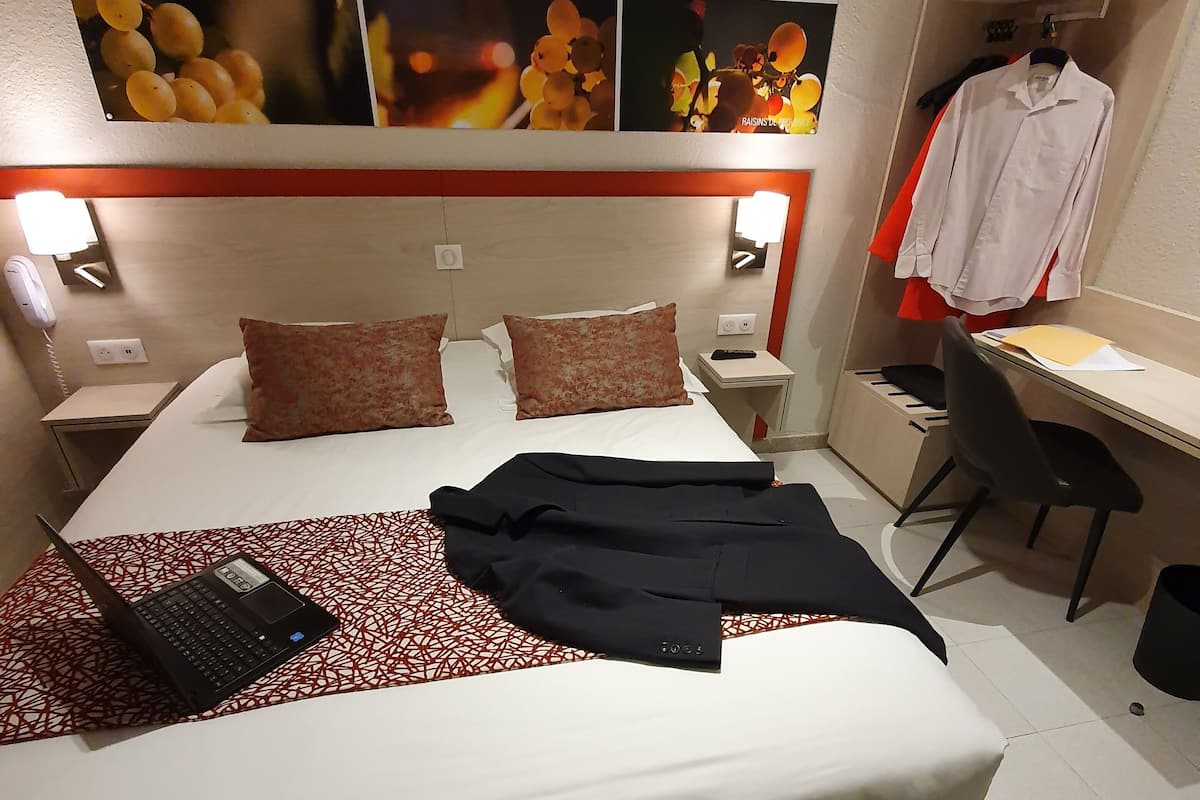 A hotel room with a bed, a desk, a chair, a phone, and a wall with fruit images.
