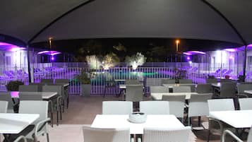 An outdoor dining area with tables and chairs, a pool, and a covered walkway.