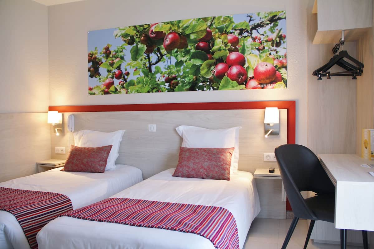 A hotel room with two beds, a desk, and a wall-mounted picture of apples.