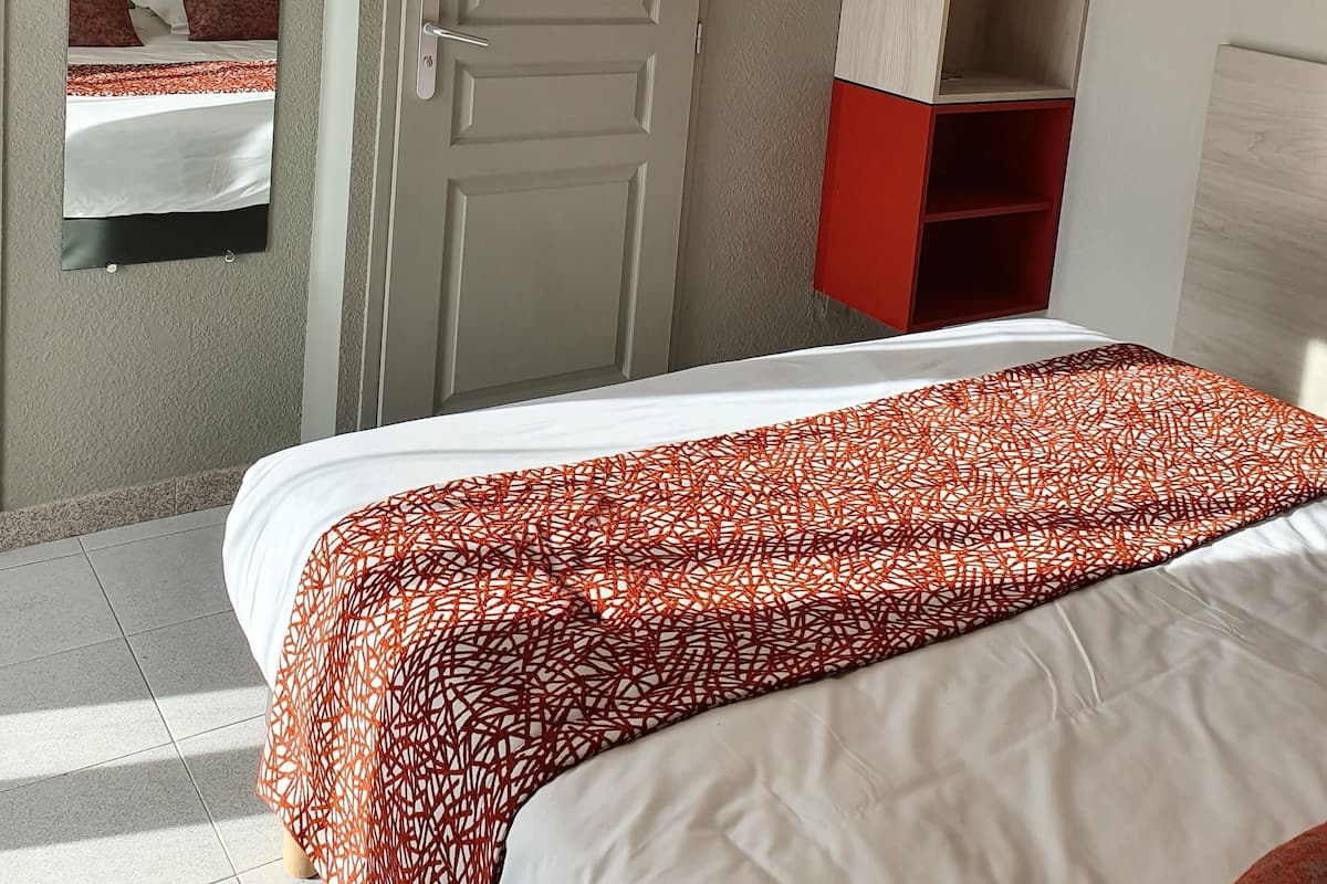 A hotel room with a bed, a door, a television, and a red storage unit.
