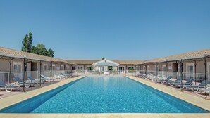 A rectangular swimming pool with lounge chairs and a covered seating area in the background. - Hotel Saint Louis (Le Thor)