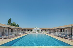 Une piscine rectangulaire, avec des chaises longues et un espace de repos couvert en arrière-plan.