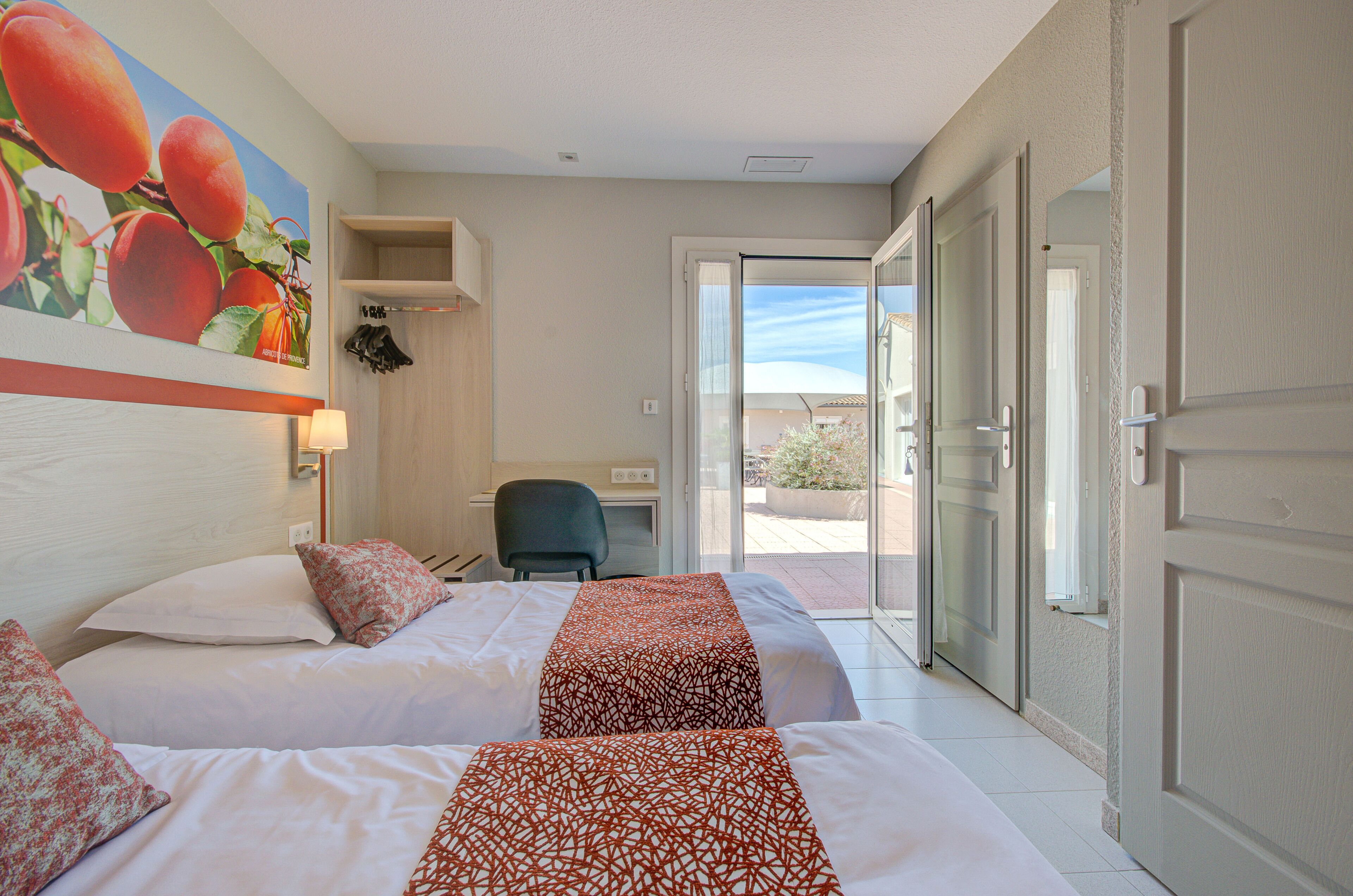 Habitación de hotel con dos camas, un escritorio y vistas a través de un ventanal.