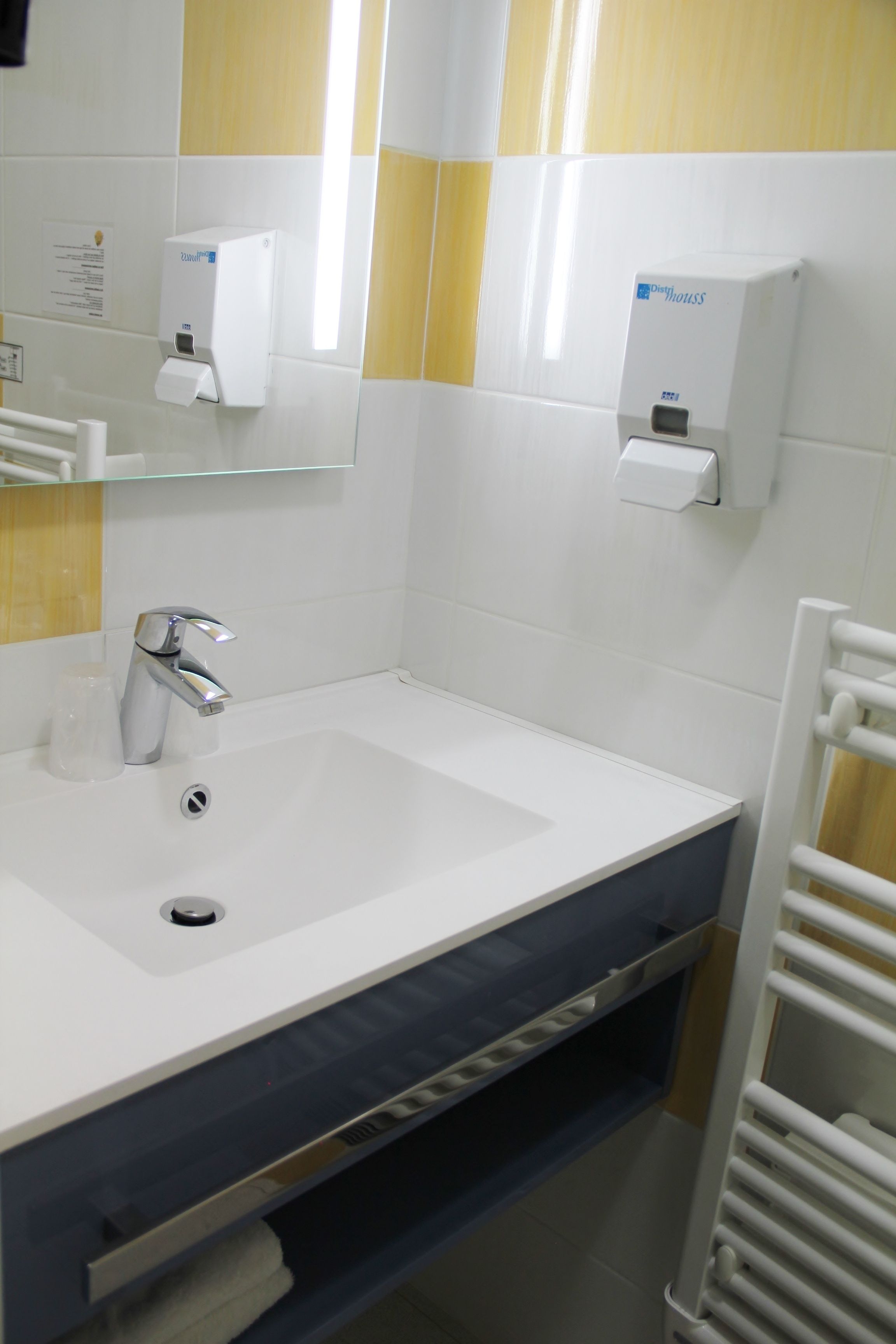 Un baño moderno con un lavamanos blanco, grifo cromado y dispensador de toallas de papel.