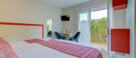 A hotel room with a bed, a desk, two chairs, a television, and a sliding door to a balcony.