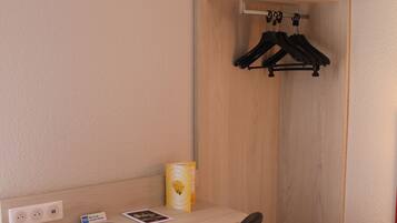Habitación compacta con escritorio, silla, perchero y un pequeño cubo de basura.