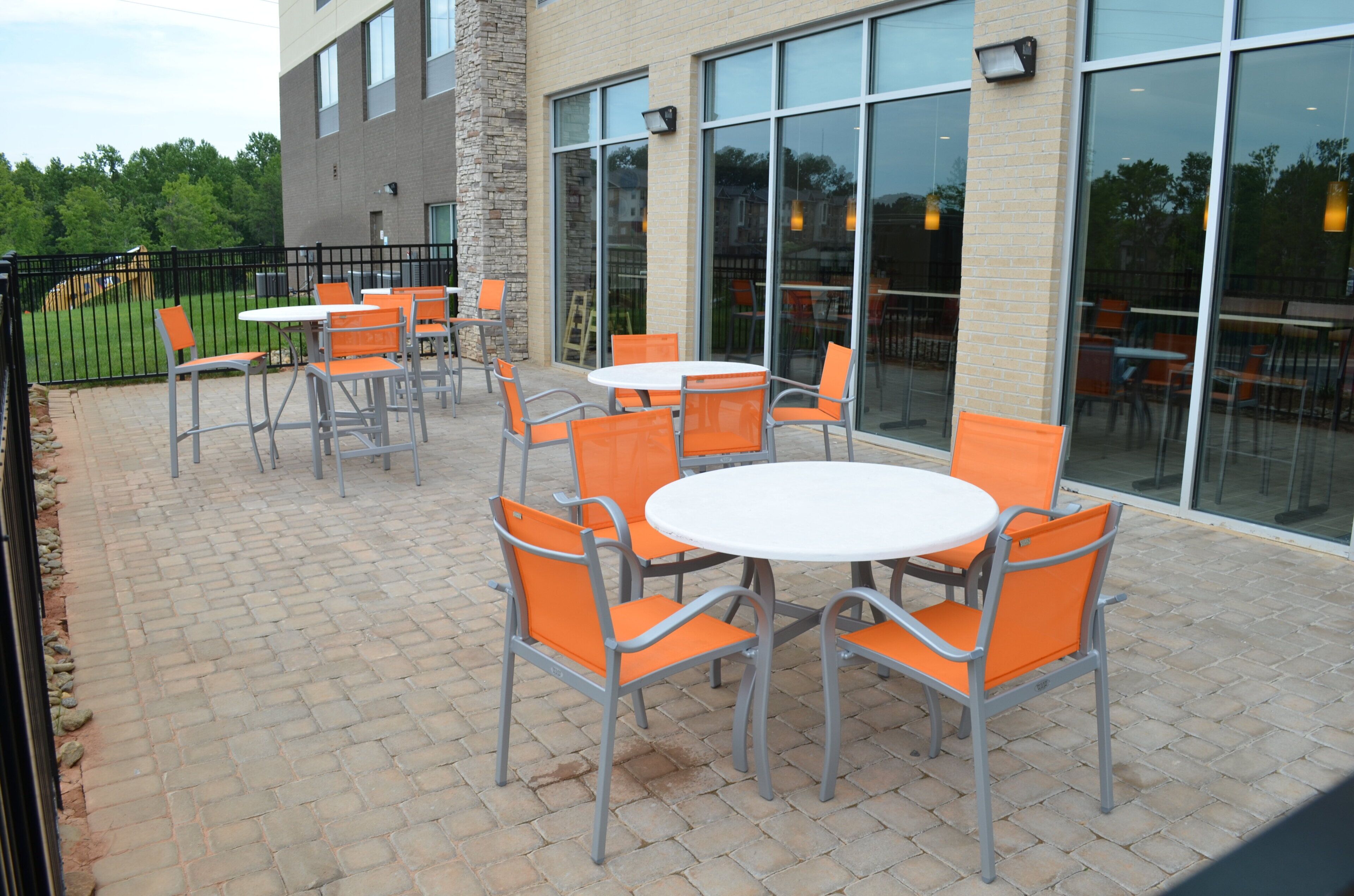 An outdoor patio area with tables and chairs, a brick floor, and a building with large windows.