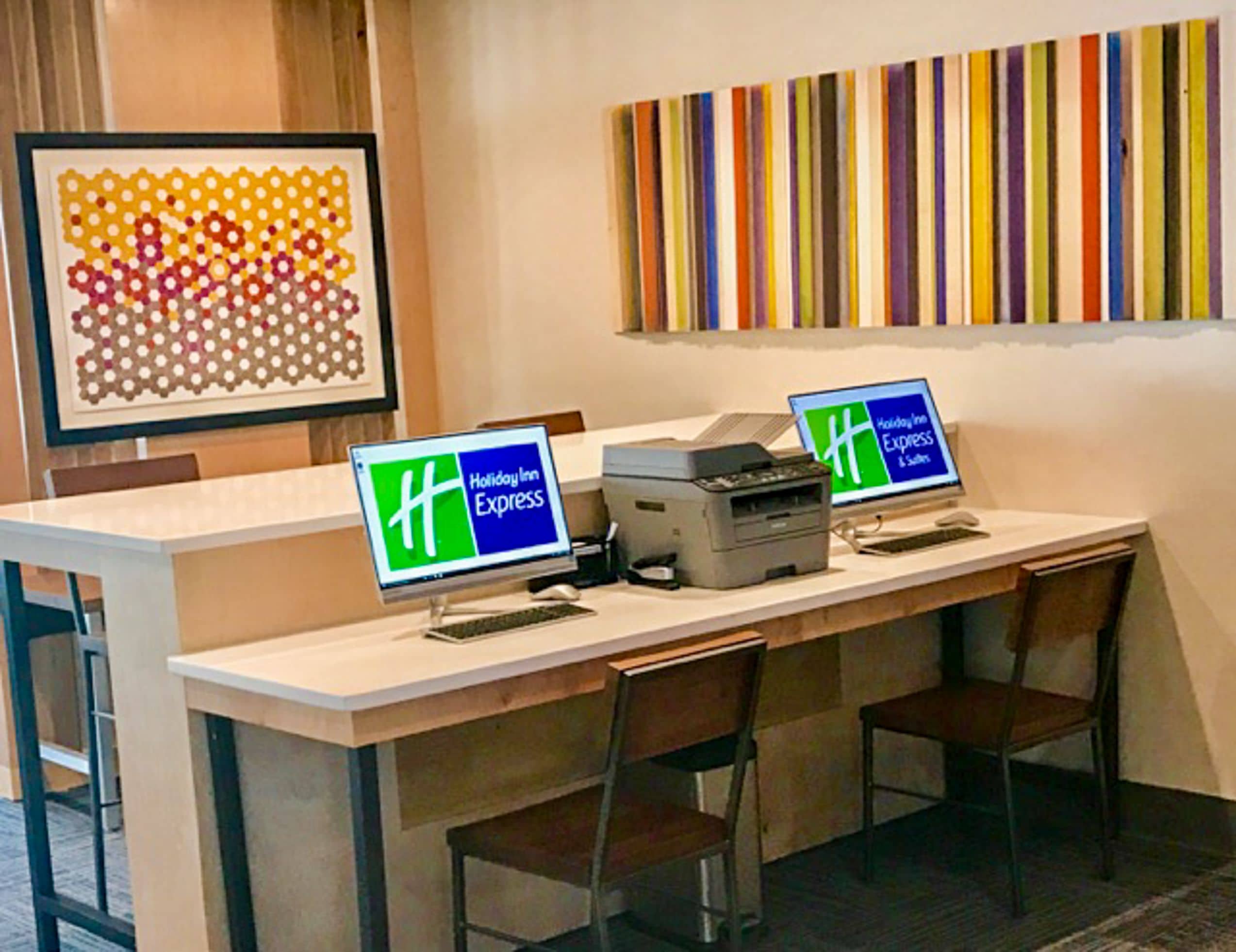 A hotel reception desk with two monitors displaying the Holiday Inn Express logo, a printer, and a framed artwork on the wall.