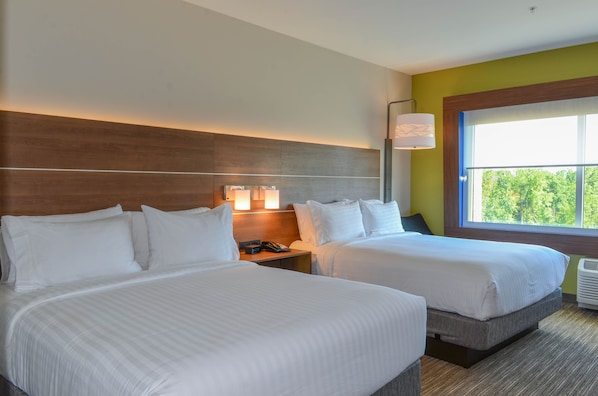 A hotel room with two beds, a nightstand with a lamp, and a window with a view of trees.