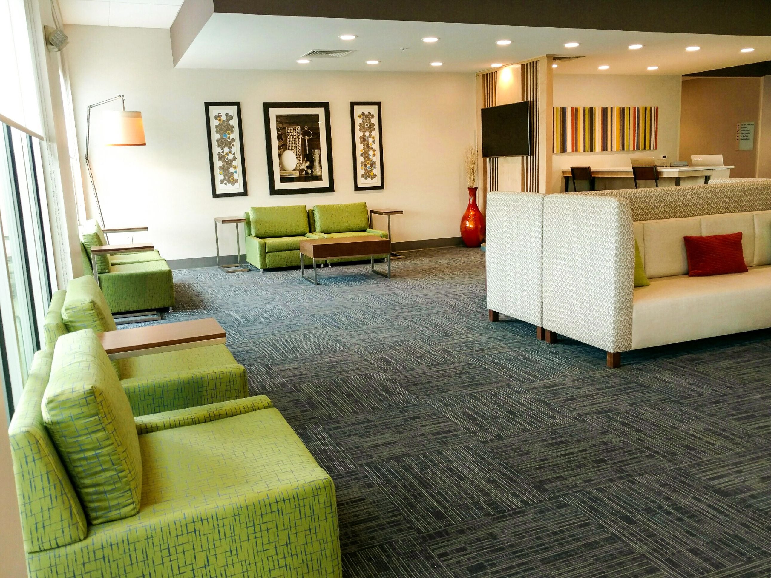 A modern lobby with green and white seating, framed artwork on the walls, and a flat-screen TV.