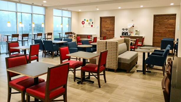 A spacious indoor dining area with multiple tables and chairs, large windows, and a modern ceiling design. - Holiday Inn Express & Suites Charlotte NE - University Area by IHG (Charlotte)