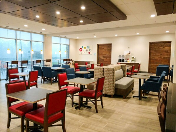 A spacious indoor dining area with multiple tables and chairs, large windows, and a modern ceiling design. - Holiday Inn Express & Suites Charlotte NE - University Area by IHG (Charlotte)