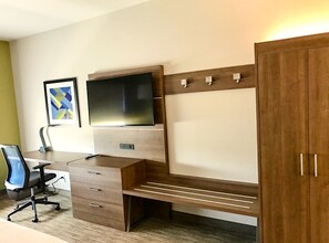 A modern bedroom with a wooden desk, a TV mounted on the wall, a wardrobe, and a framed picture. - Holiday Inn Express & Suites Charlotte NE - University Area by IHG (Charlotte)