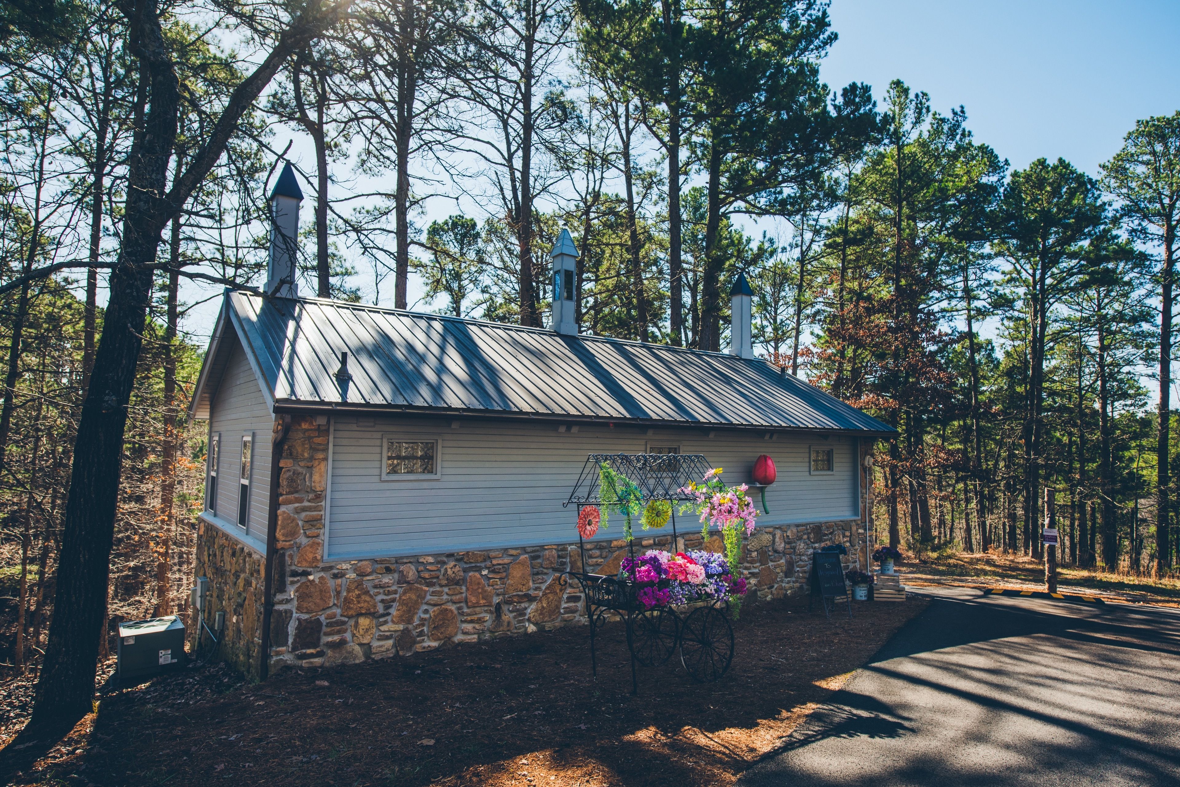 A small stone and metal building with a metal roof, surrounded by trees.