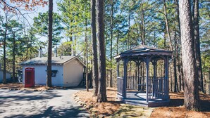 A gazebo with a wooden railing and a small porch, surrounded by trees. - Hogsveil Cottages - Harry Potter Themed (Eureka Springs)