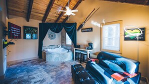 A cozy room with a stone floor, a black leather sofa, a wooden ceiling, a ceiling fan, a fireplace, and a sign that says "Hogsweel". - Hogsveil Cottages - Harry Potter Themed (Eureka Springs)
