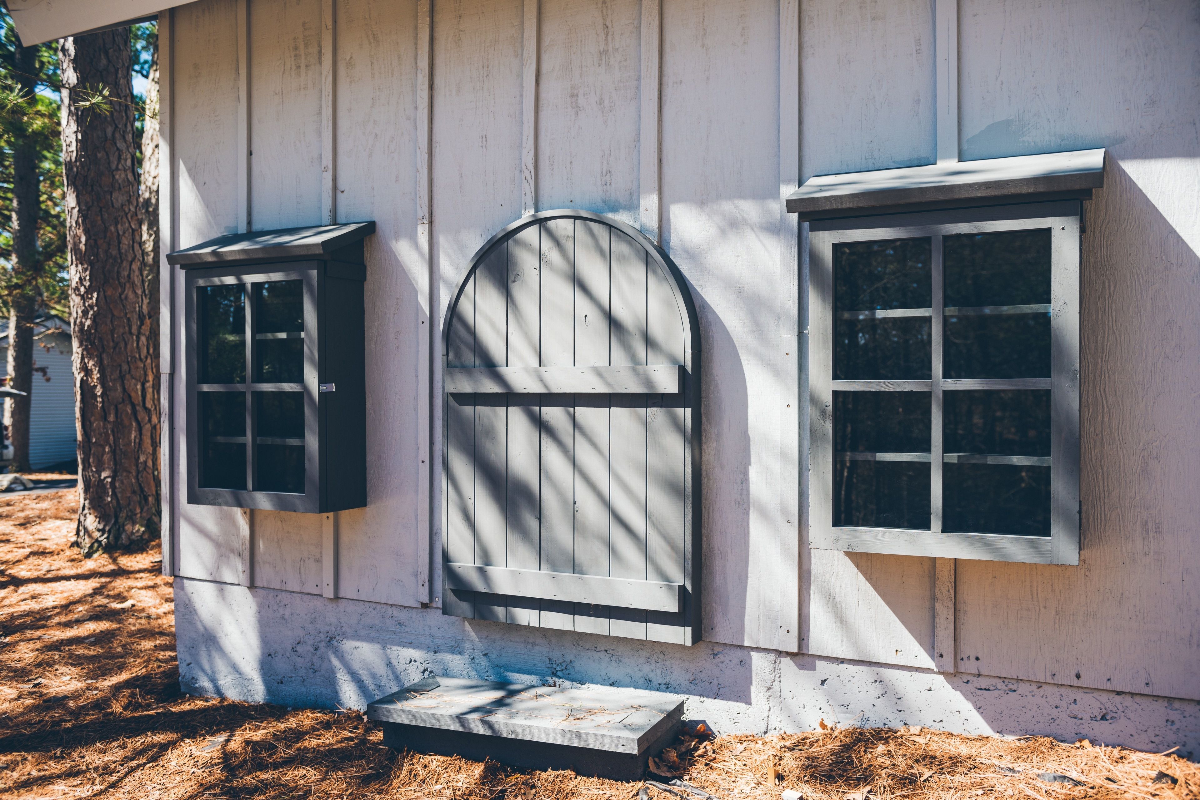 A wooden building with three windows, one arched and two rectangular, and a small step leading to the entrance.