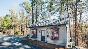 A small, single-story cabin with a dark door and purple-framed windows, surrounded by a forest. - Hogsveil Cottages - Harry Potter Themed (Eureka Springs)
