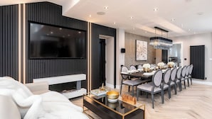 Una sala de estar moderna con chimenea, un comedor con una mesa larga y un televisor montado en la pared.
