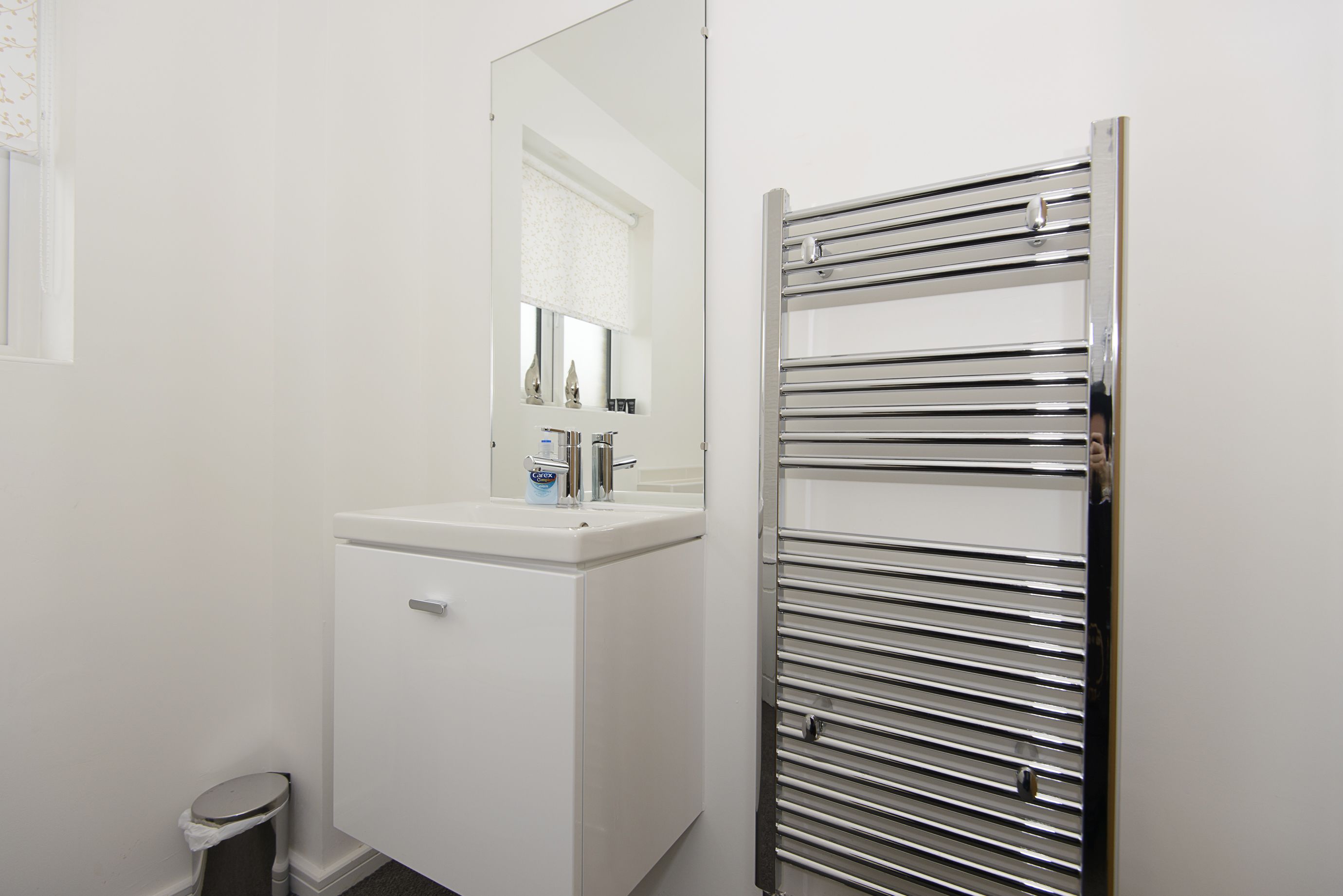 A bathroom with a white sink, mirror, and chrome towel rack.