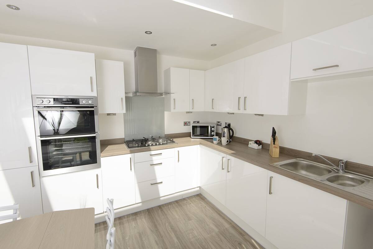 A modern kitchen with white cabinets, a double oven, a stove, a microwave, and a sink.
