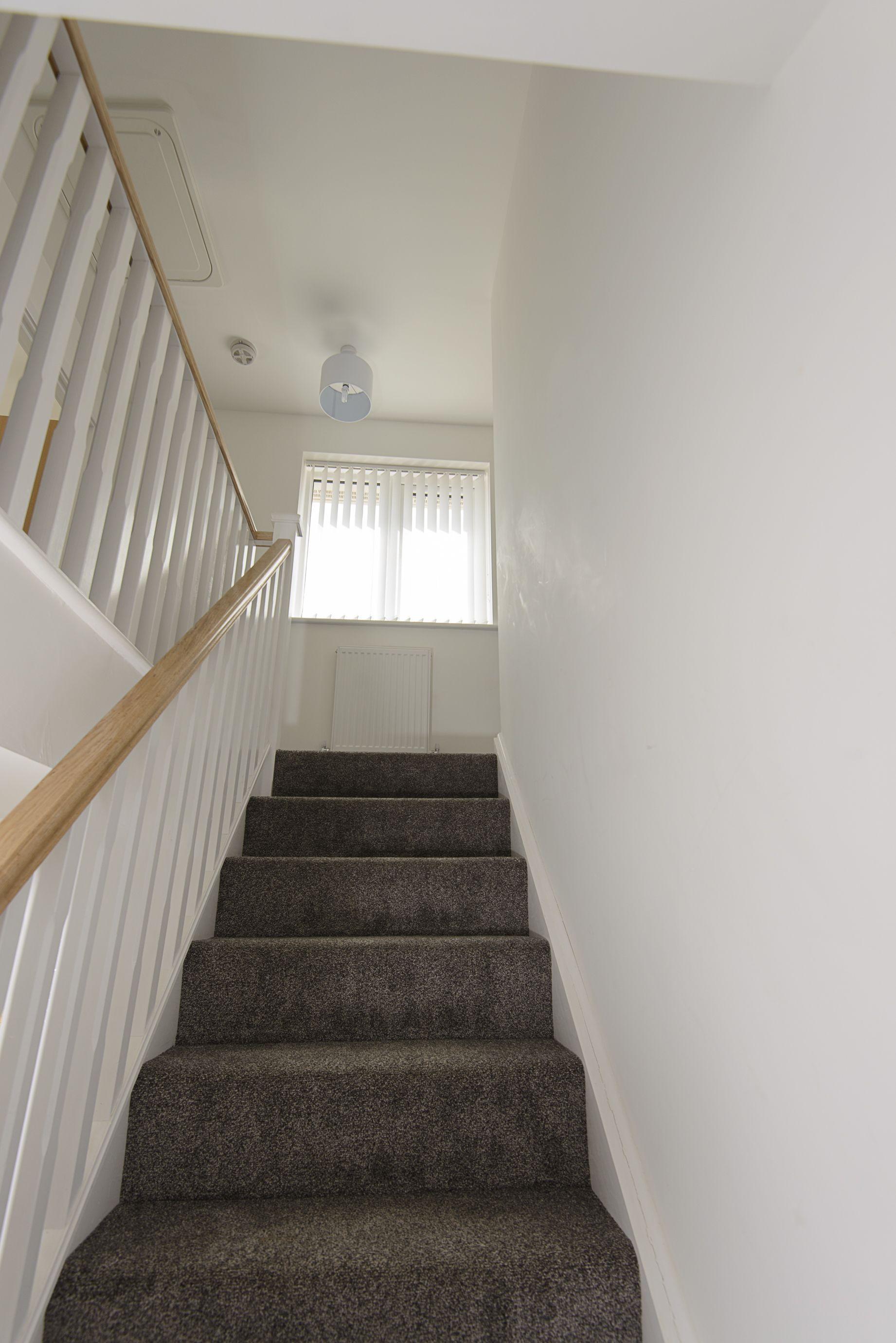 A staircase with wooden handrails and carpeted steps leading to a landing with a white door and a window with blinds.
