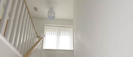 A staircase with wooden handrails and carpeted steps leading to a landing with a white door and a window with blinds.