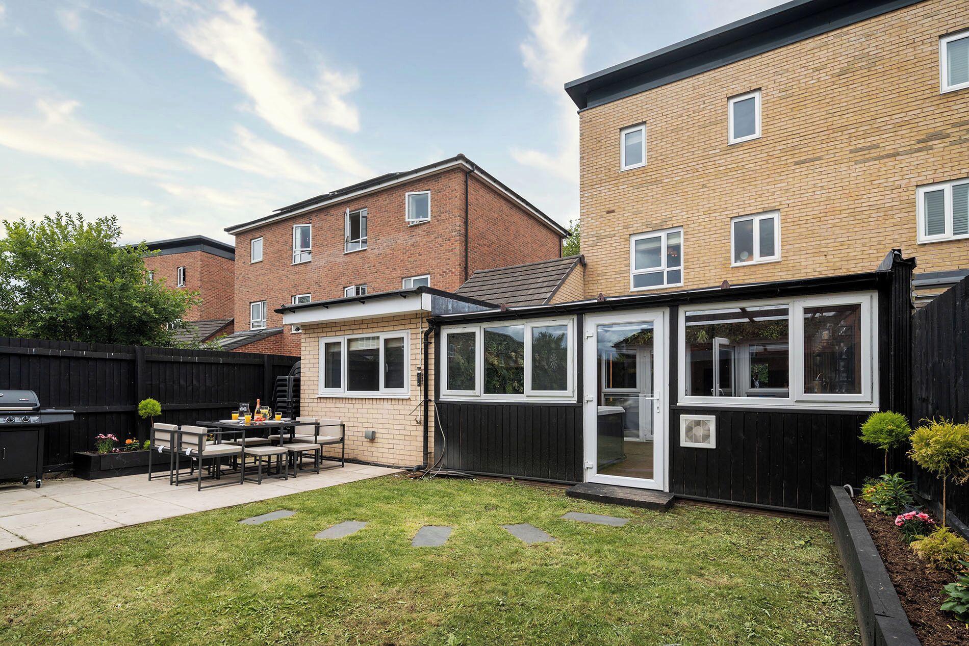A residential backyard with a patio, a barbecue grill, and a small garden area.