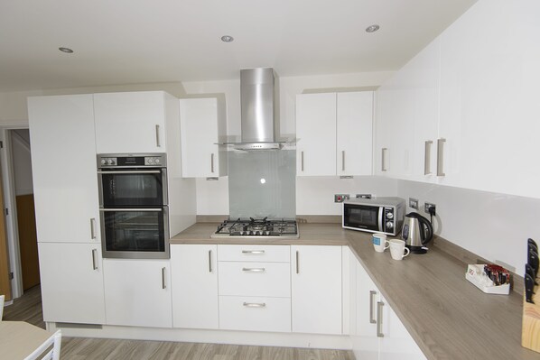 A modern kitchen with white cabinets, a built-in oven, a stove, a microwave, and a coffee maker.
